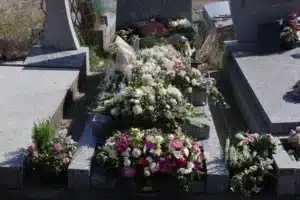 Allée de tombeau ornée de bouquets funéraires colorés sur une pierre tombale entourée d’autres monuments funéraires.