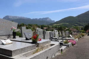 Allée de tombes en pierre au cimetière, fleurs et monuments gravés, montagnes en arrière-plan sous ciel clair. intégrant le sujet : comment nettoyer la tombe d'un proche.