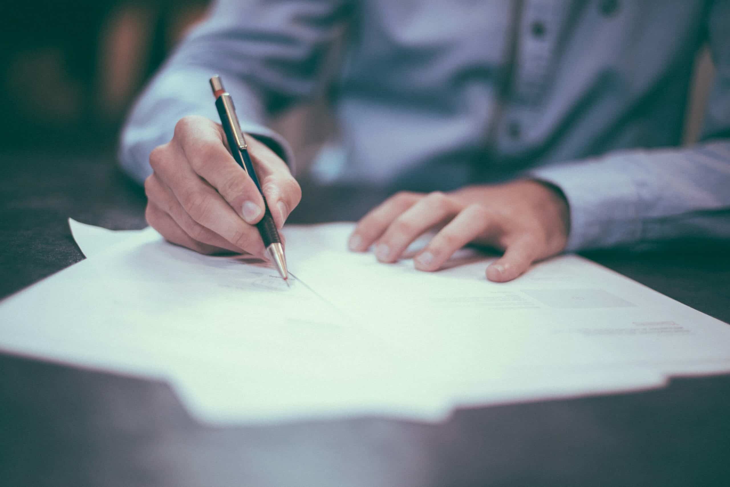 Personne signant un document sur une table, en lumière douce, prêt à gérer les aspects juridiques et financiers liés à la succession et aux frais d’obsèques. commentaire: comment la succession finance les frais d'obsèques.