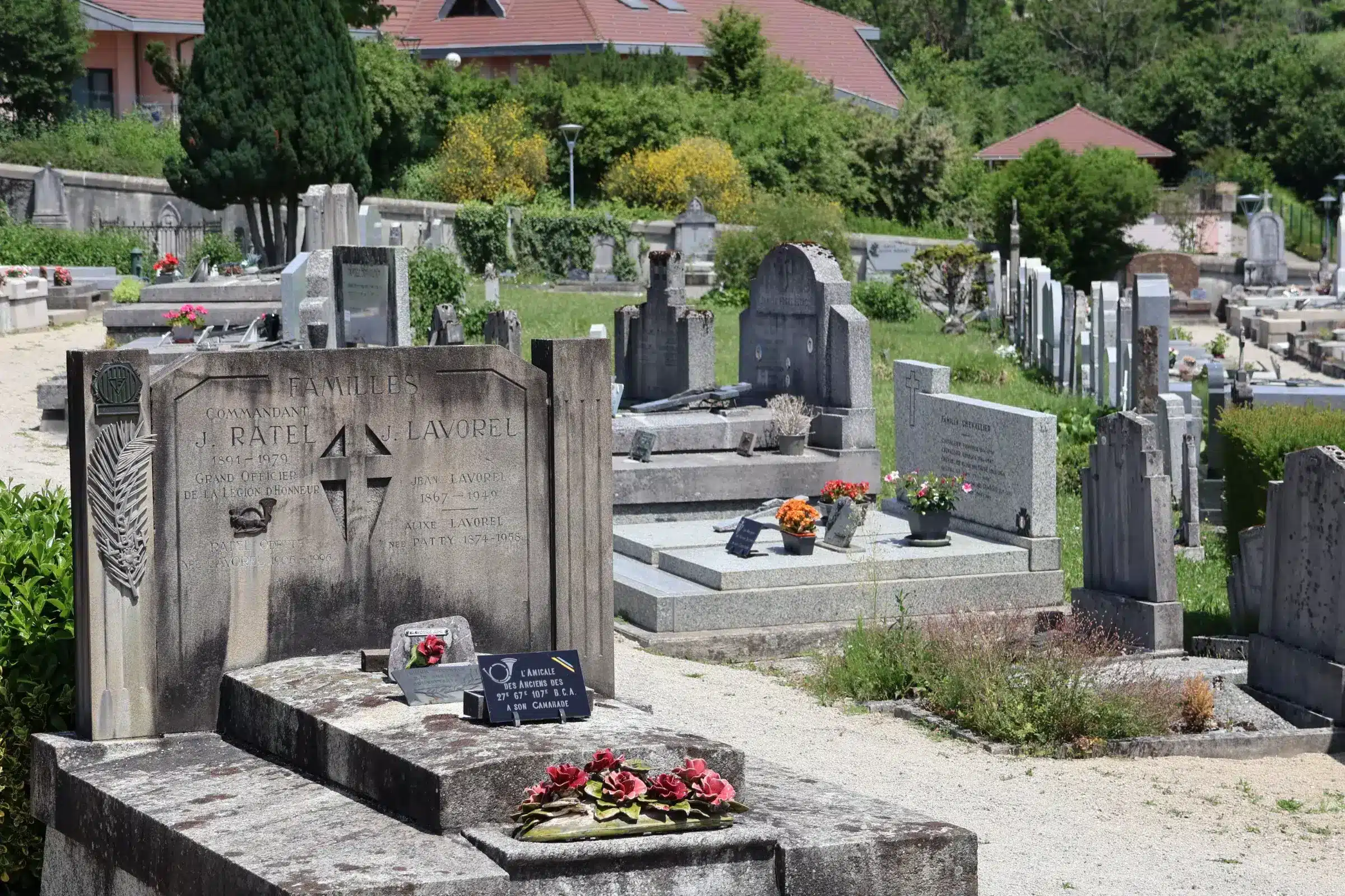 Tombe et sépultures dans un cimetière bien entretenu, graves alignées et récemment fleuries, avec verdure et jardins autour. Anticiper frais entretien sépulture au centre.