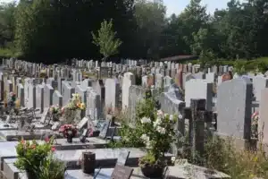 Vue d’un cimetière avec des tombes en pierre, fleurs et bouquets, allées ombragées et gazon autour des monuments funéraires. droits succession entretien tombe