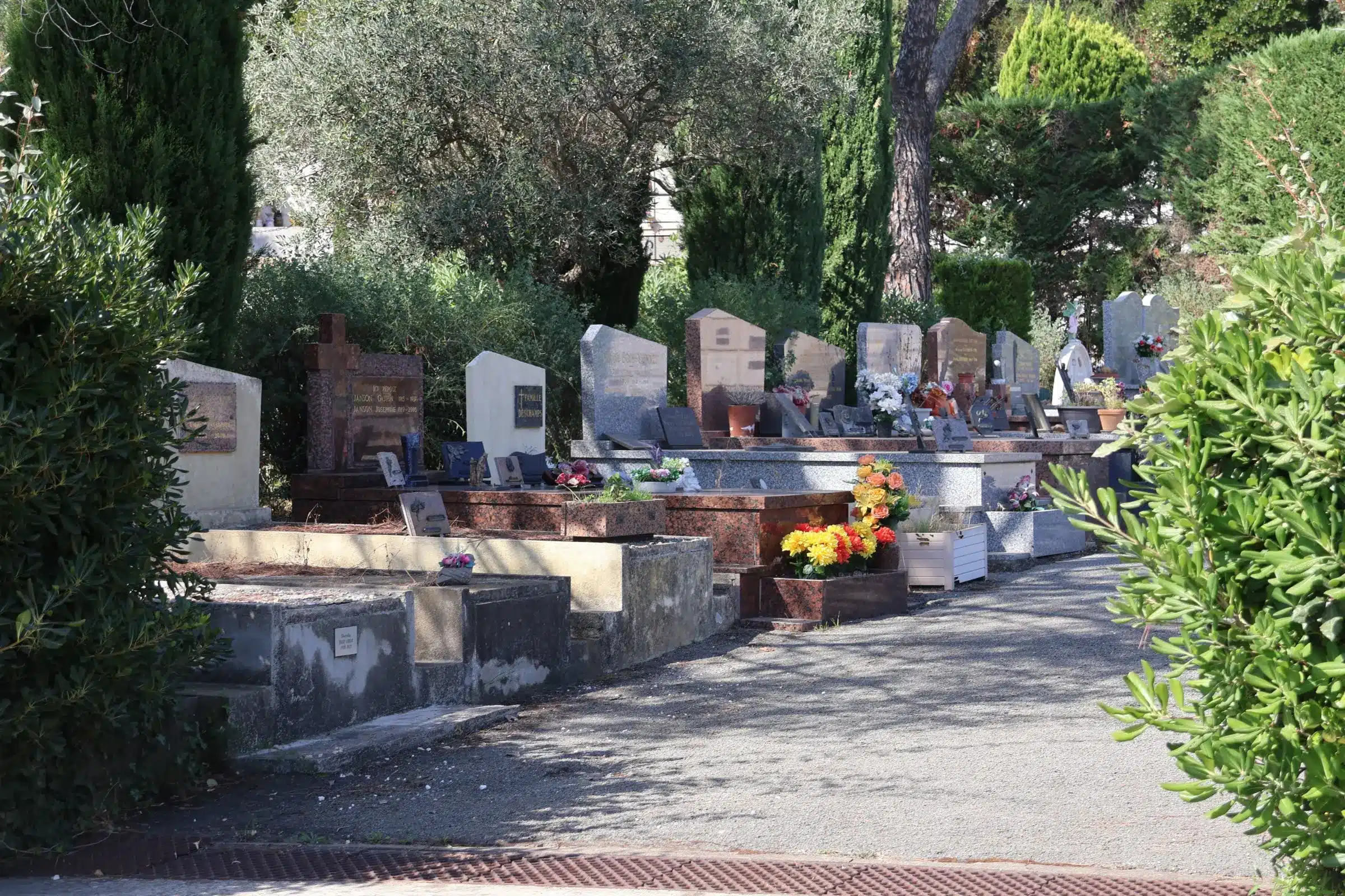 Allée de tombes alignées dans un cimetière, avec pierres tombales, fleurs et arbustes verts. Allée de tombes alignées dans un cimetière, avec pierres tombales, fleurs et arbustes verts.