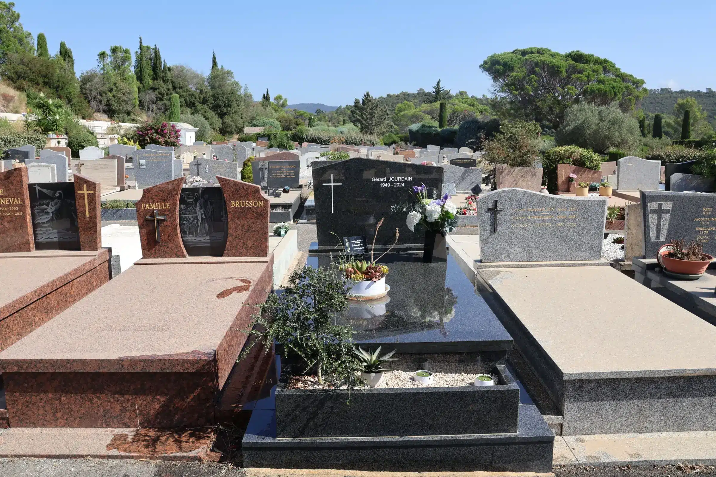 Tombeau familial en pierre sombre, entourée de grandes stèles funéraires dans un cimetière plein soleil, avec des vases de Tombeau familial en pierre sombre, entourée de grandes stèles funéraires dans un cimetière plein soleil, avec des vases de