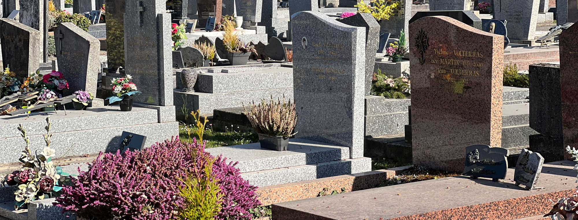 Vignete d’un cimetière avec des tombes en pierre et des fleurs colorées.